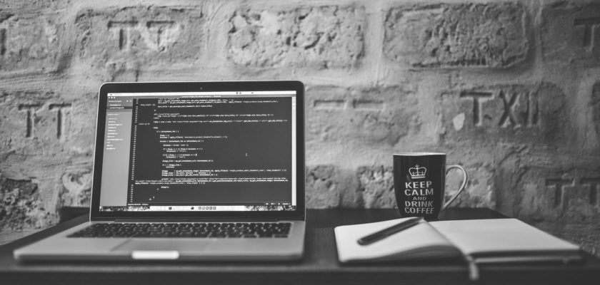 grayscale photo of computer laptop near white notebook and ceramic mug on table